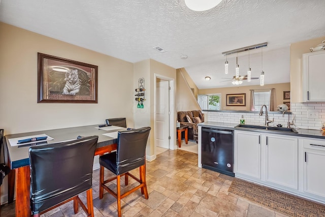 kitchen featuring white cabinets, a sink, dishwasher, decorative backsplash, and visible vents