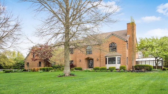 view of front facade with brick siding, a front yard, and a chimney