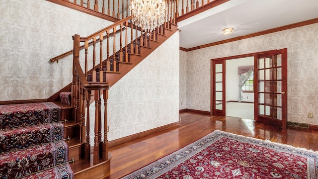 staircase featuring french doors, wallpapered walls, a chandelier, and wood finished floors
