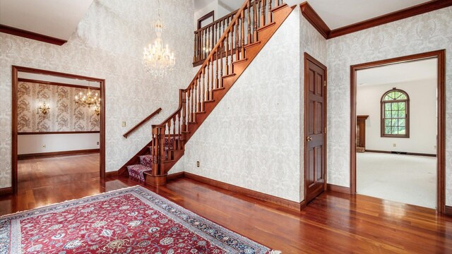 staircase featuring an inviting chandelier, ornamental molding, wood finished floors, and wallpapered walls