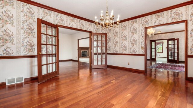 unfurnished dining area featuring visible vents, an inviting chandelier, wood finished floors, wallpapered walls, and french doors