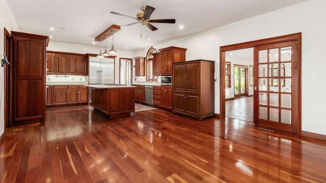 kitchen featuring a ceiling fan, a kitchen island, light countertops, built in appliances, and dark wood-type flooring