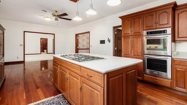 kitchen with a kitchen island, a ceiling fan, light countertops, stainless steel appliances, and dark wood-type flooring