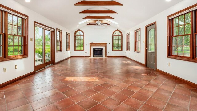 unfurnished living room with a ceiling fan, baseboards, vaulted ceiling with beams, dark tile patterned flooring, and a fireplace with flush hearth