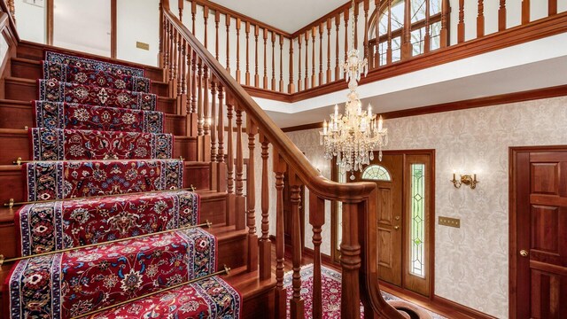 stairway with crown molding, a towering ceiling, a notable chandelier, and wallpapered walls