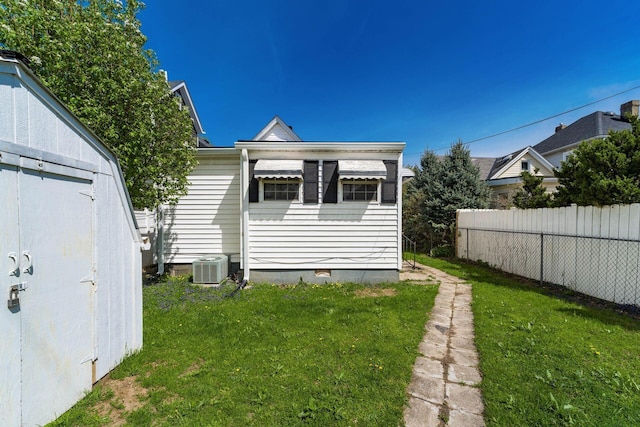 rear view of house with central AC, fence, a yard, and crawl space