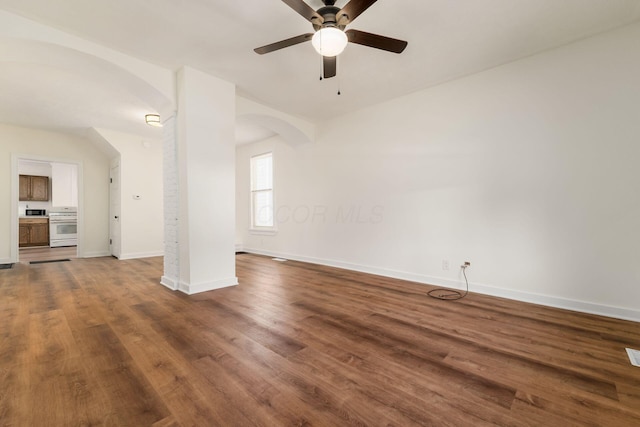 unfurnished living room with arched walkways, baseboards, a ceiling fan, and wood finished floors