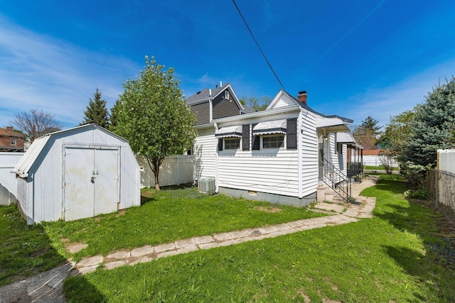 rear view of property featuring a yard, a chimney, a fenced backyard, and a storage unit