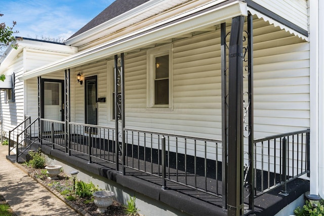 doorway to property featuring covered porch and a shingled roof