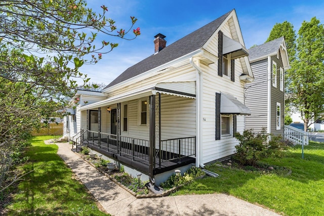 view of side of property with roof with shingles, fence, a chimney, a lawn, and covered porch