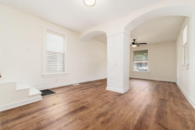 empty room featuring baseboards, arched walkways, decorative columns, and wood finished floors