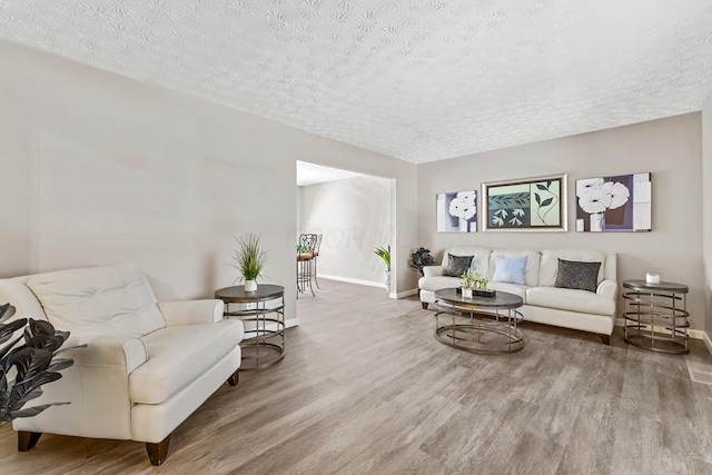 living area with a textured ceiling, baseboards, and wood finished floors