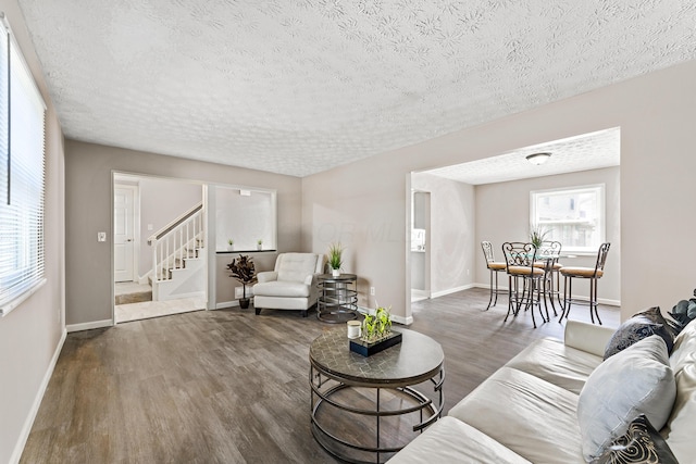 living area featuring stairs, baseboards, a textured ceiling, and wood finished floors