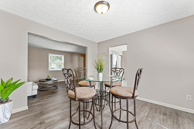 dining area featuring a textured ceiling, baseboards, and wood finished floors