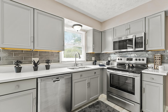 kitchen with a sink, gray cabinets, a textured ceiling, and stainless steel appliances