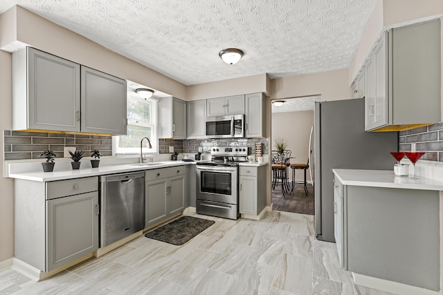 kitchen featuring gray cabinetry, appliances with stainless steel finishes, decorative backsplash, and a sink
