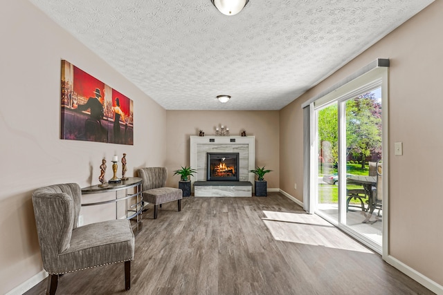sitting room featuring a glass covered fireplace, a textured ceiling, baseboards, and wood finished floors