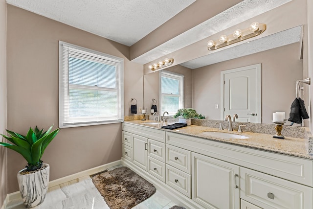 bathroom with a sink, baseboards, a textured ceiling, and double vanity