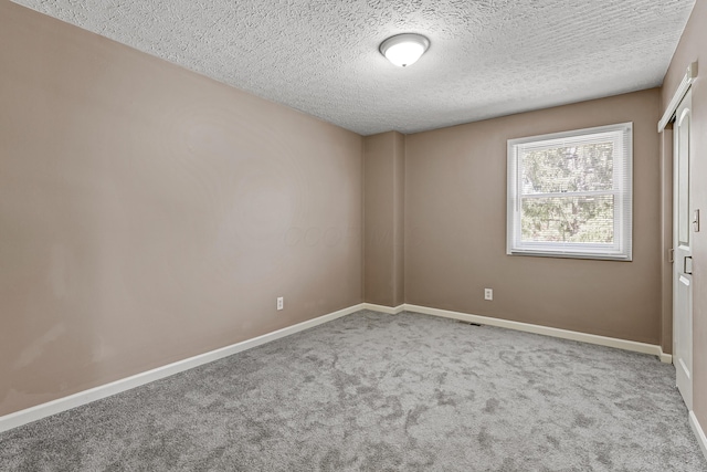 spare room with a textured ceiling, baseboards, and carpet