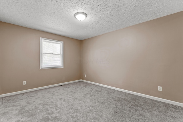 carpeted spare room featuring a textured ceiling and baseboards