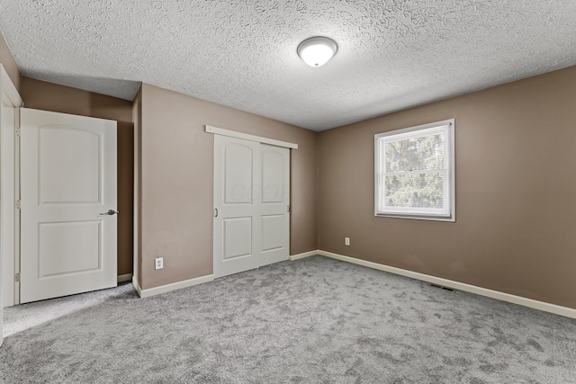 unfurnished bedroom with a textured ceiling, visible vents, carpet floors, baseboards, and a closet
