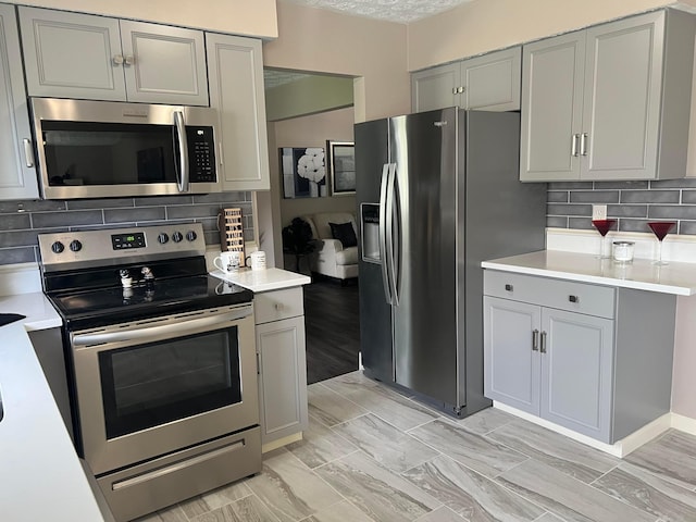 kitchen featuring light countertops, stainless steel appliances, gray cabinets, and backsplash