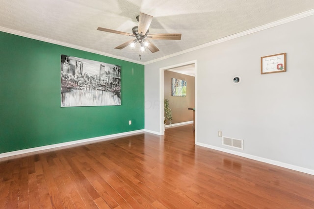empty room featuring ceiling fan, visible vents, wood finished floors, baseboards, and ornamental molding