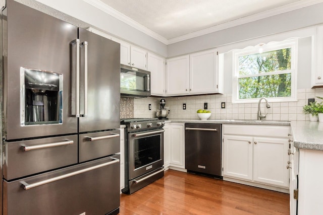 kitchen with wood finished floors, white cabinetry, a sink, backsplash, and stainless steel appliances