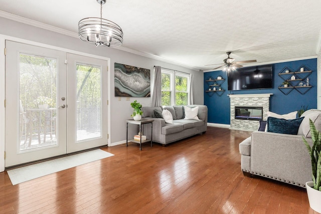 living area with ornamental molding, a stone fireplace, hardwood / wood-style flooring, french doors, and ceiling fan with notable chandelier