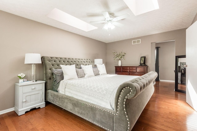 bedroom featuring ceiling fan, visible vents, a skylight, wood finished floors, and baseboards