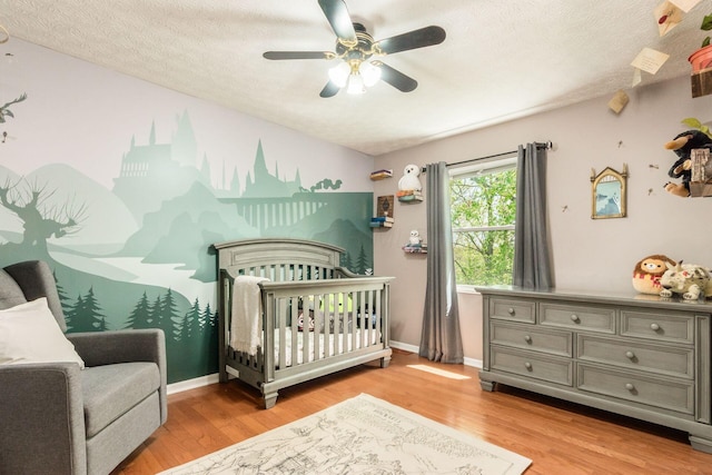 bedroom featuring a textured ceiling, a crib, ceiling fan, and wood finished floors