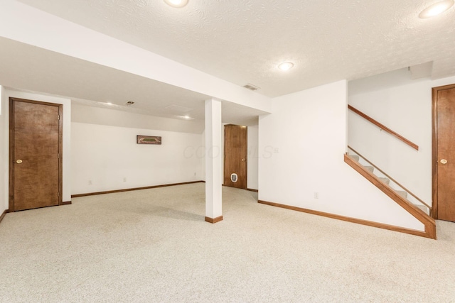 finished below grade area with baseboards, a textured ceiling, stairs, and light carpet