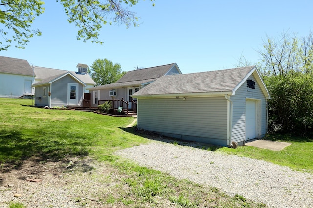 rear view of property featuring a wooden deck, roof with shingles, an outbuilding, a yard, and a detached garage