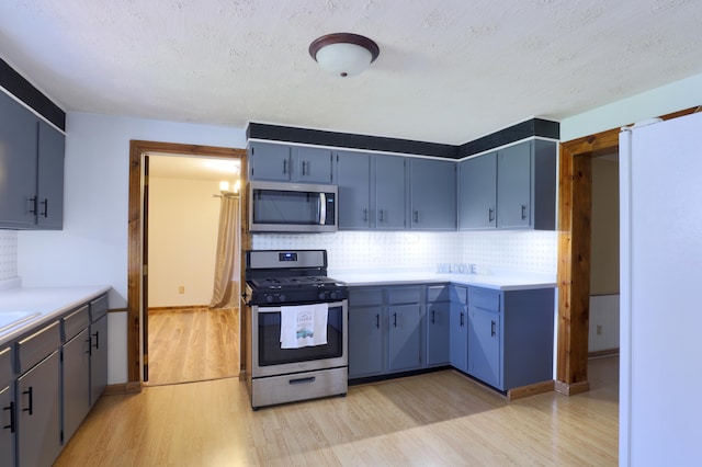 kitchen featuring decorative backsplash, light countertops, blue cabinets, light wood finished floors, and appliances with stainless steel finishes
