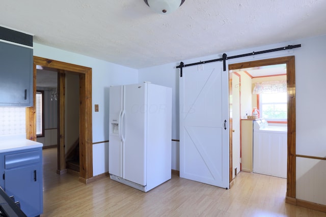 interior space with blue cabinets, a textured ceiling, light countertops, white fridge with ice dispenser, and light wood-style flooring