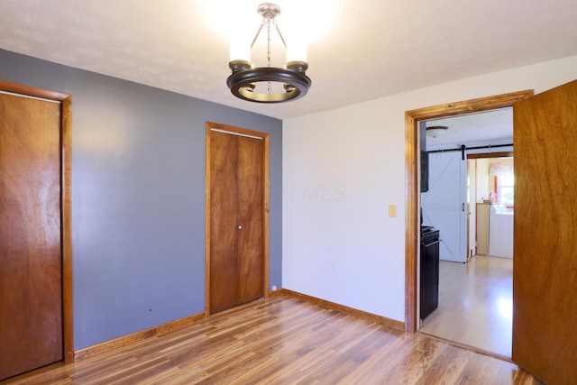 unfurnished bedroom with baseboards, light wood finished floors, a barn door, and a chandelier