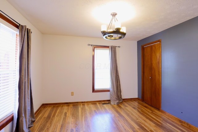 spare room with a healthy amount of sunlight, baseboards, wood finished floors, and a notable chandelier