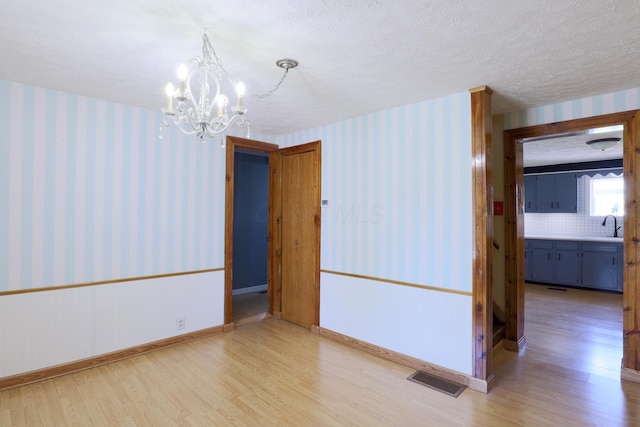empty room with wallpapered walls, an inviting chandelier, a sink, and light wood finished floors