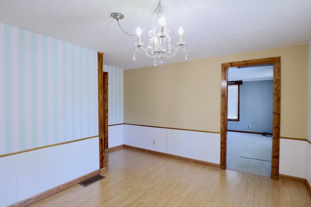 empty room featuring visible vents, wood finished floors, baseboards, a textured ceiling, and a chandelier