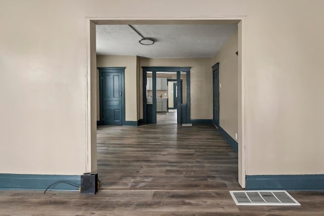 hall with visible vents, dark wood-style flooring, and baseboards