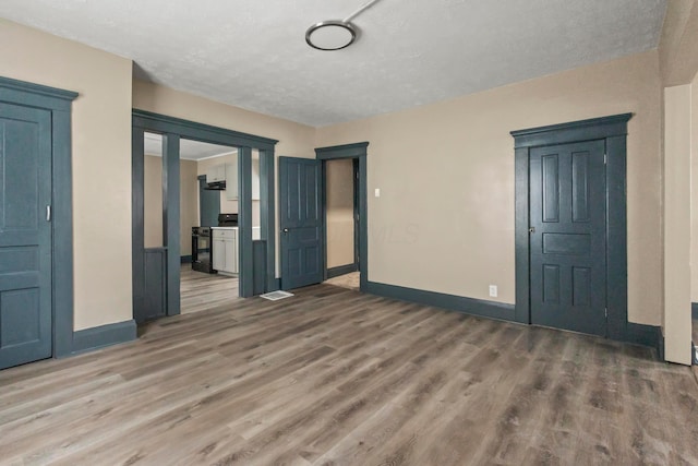 spare room with a textured ceiling, baseboards, and wood finished floors
