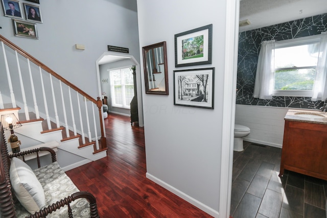 interior space featuring wallpapered walls, baseboards, an accent wall, wood finished floors, and arched walkways