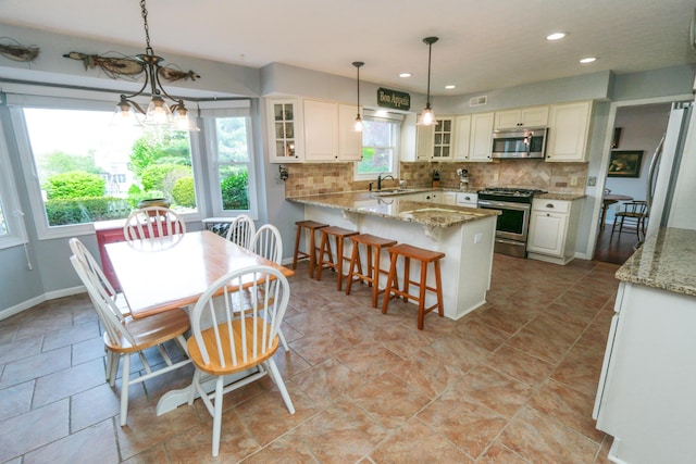 kitchen featuring a peninsula, glass insert cabinets, appliances with stainless steel finishes, and decorative backsplash