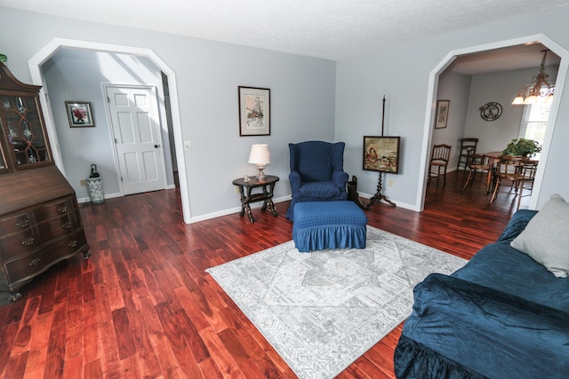 living area featuring arched walkways, baseboards, a chandelier, and wood finished floors