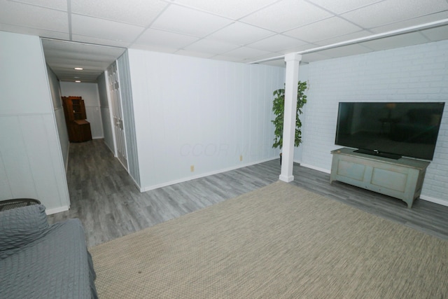 unfurnished living room with a paneled ceiling, baseboards, and wood finished floors