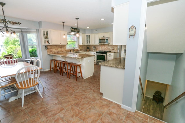 kitchen with glass insert cabinets, a sink, a peninsula, backsplash, and appliances with stainless steel finishes