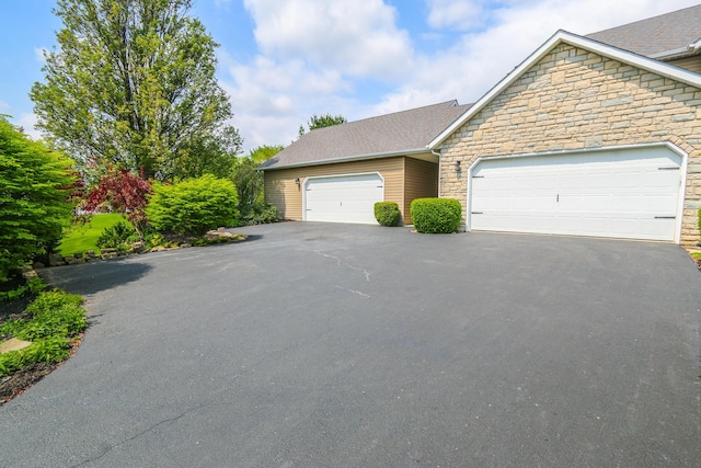 view of front of property with stone siding, a shingled roof, driveway, and a garage