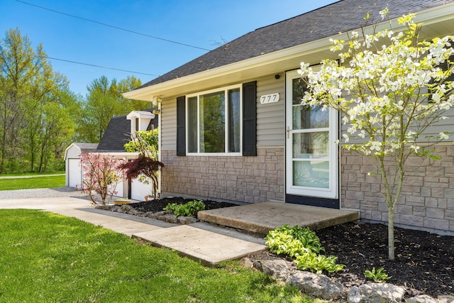 view of exterior entry featuring a yard, roof with shingles, stone siding, and a garage
