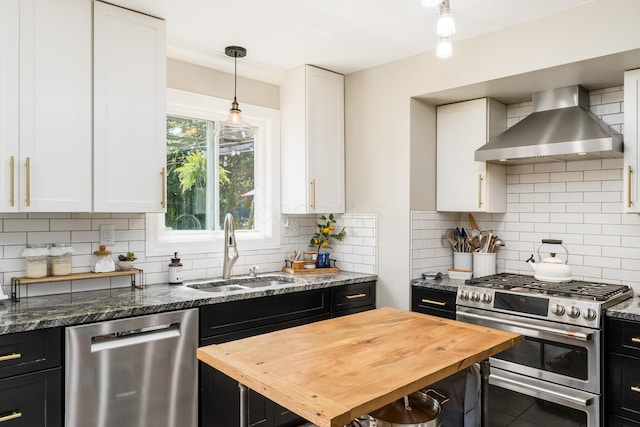 kitchen with wall chimney range hood, a sink, dark cabinetry, wood counters, and stainless steel appliances