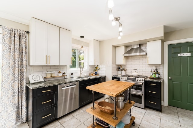 kitchen with wall chimney range hood, stainless steel appliances, a sink, and white cabinetry